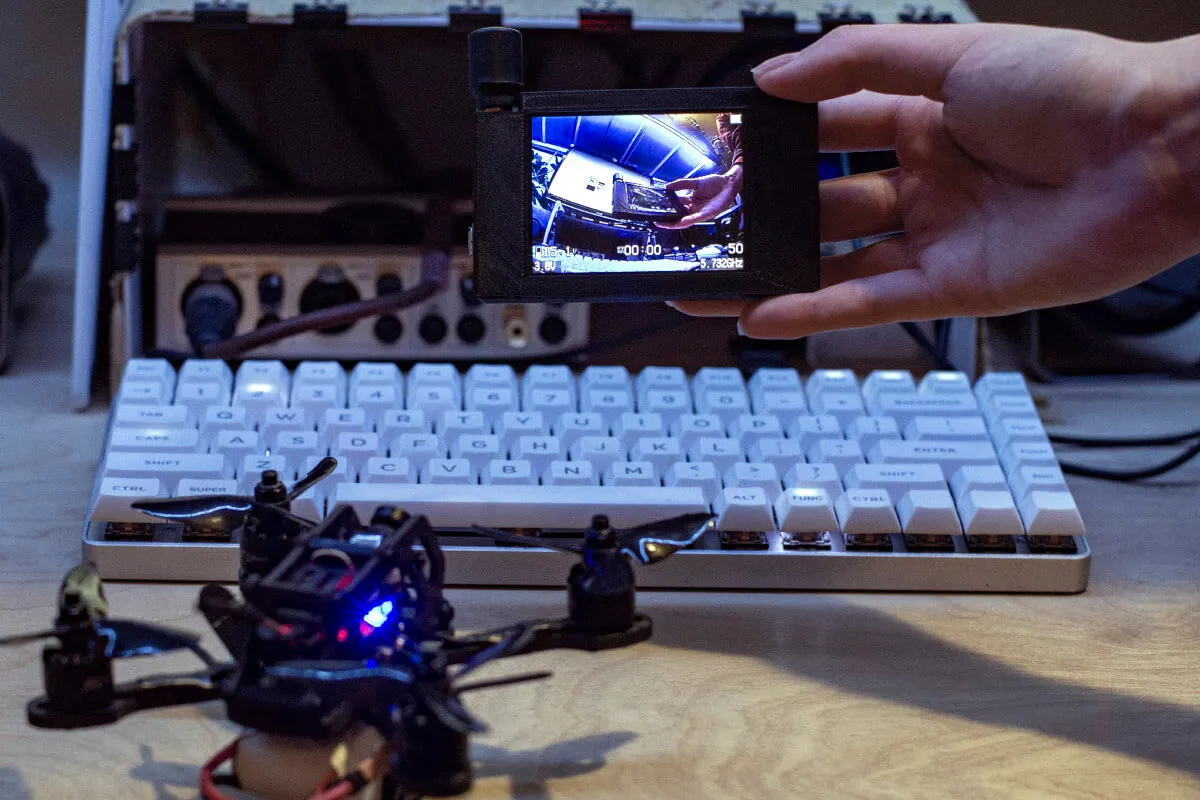 Final assembly shown displaying live FPV feed from a drone on the desk.